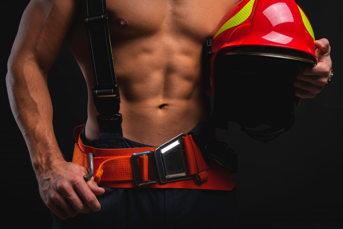 Muscular,,handsome,young,firefighter,on,dark,background,holding,fire,helmet,